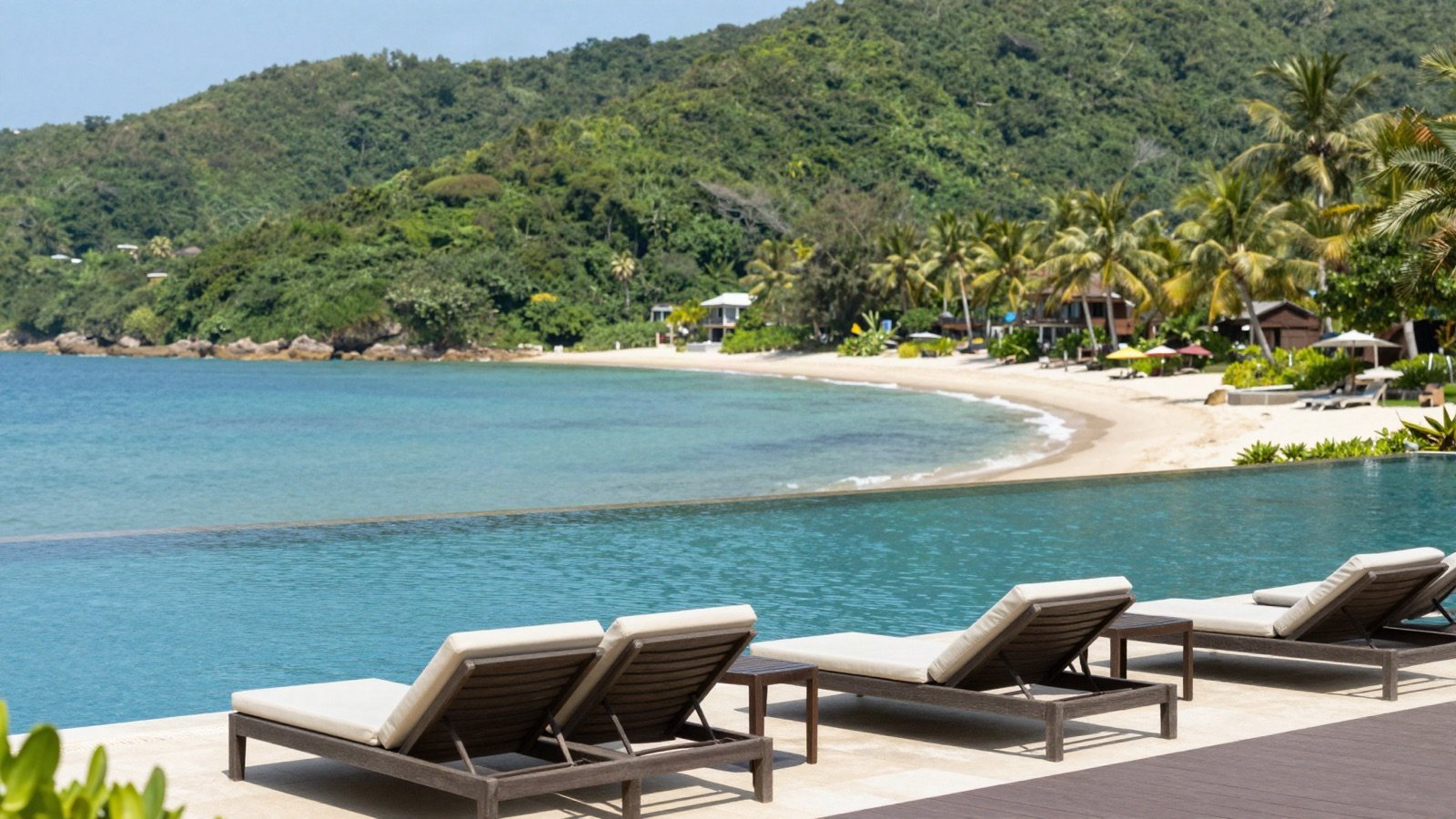 Infinity pool with sun loungers above a tropical bay